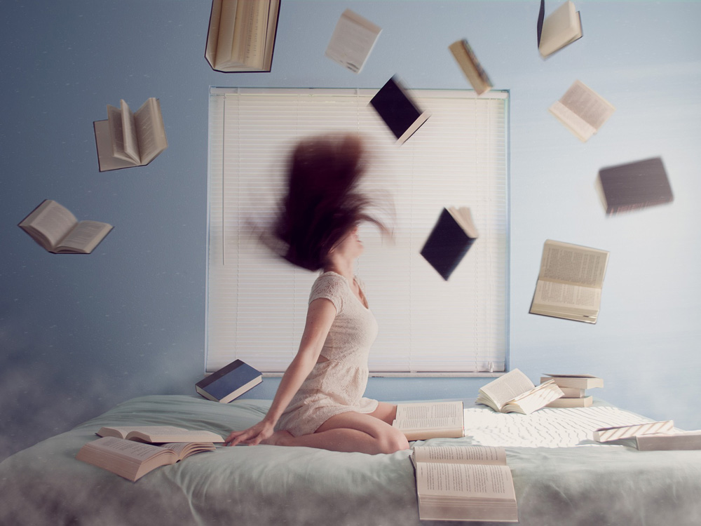 Symbolbild Frau auf Bett mit um sie herumfliegenden Büchern